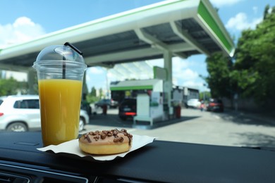 Photo of Plastic cup of juice and doughnut on car dashboard at gas station. Space for text