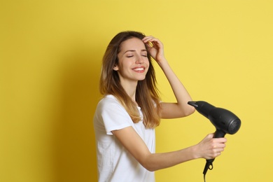 Photo of Beautiful young woman using hair dryer on yellow background