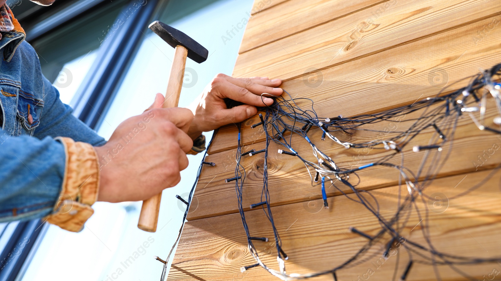 Photo of Man decorating house with Christmas lights outdoors, closeup