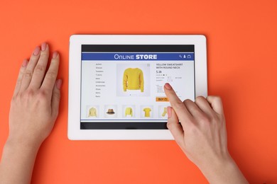 Photo of Woman with tablet shopping online on orange background, top view