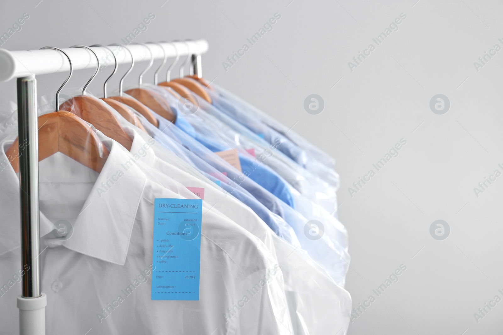 Photo of Rack with clean clothes on hangers after dry-cleaning against light background