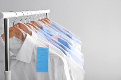 Rack with clean clothes on hangers after dry-cleaning against light background