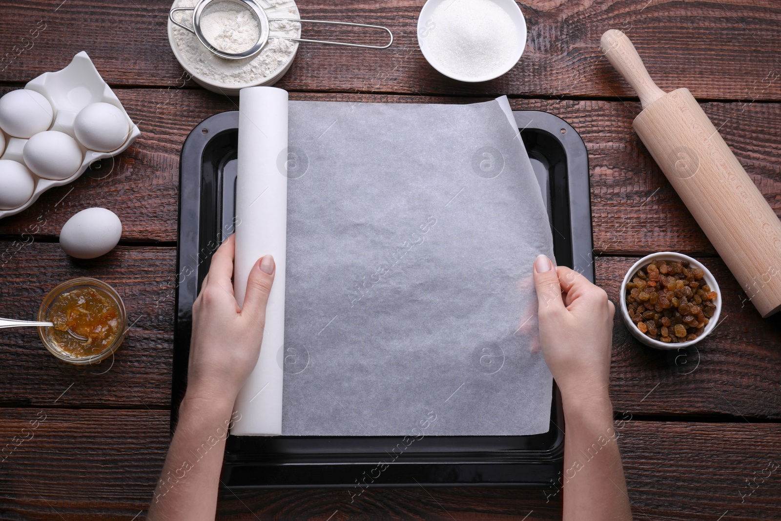 Photo of Woman putting parchment paper in baking pan at wooden table, top view