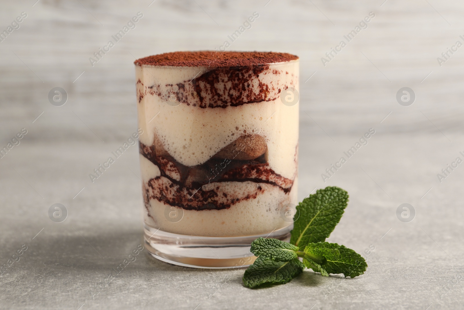 Photo of Delicious tiramisu in glass and mint on grey textured table, closeup