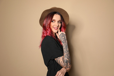 Photo of Beautiful woman with tattoos on arms against beige background