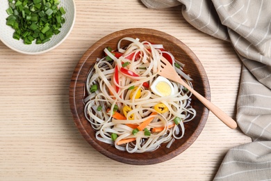 Photo of Bowl of noodles with broth, vegetables and egg on wooden background, top view