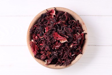 Photo of Dry hibiscus tea in bowl on white wooden table, top view