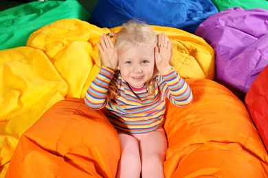 Photo of Cute child playing on colorful bean bag chairs indoors
