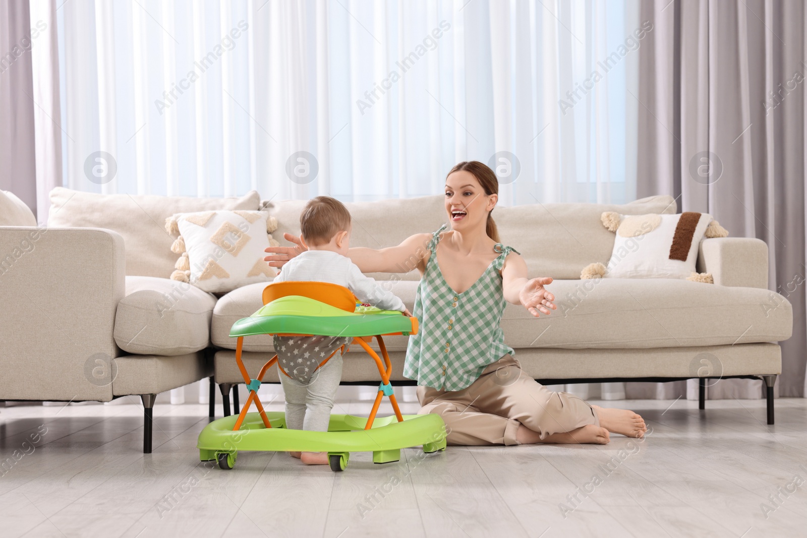 Photo of Little boy in baby walker hurrying to happy mother at home. Woman calling child with open arms