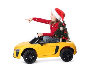 Photo of Cute little girl in Santa hat with Christmas tree driving children's electric toy car on white background