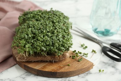 Photo of Fresh daikon radish microgreen and scissors on white marble table, closeup. Space for text