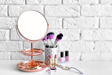 Photo of Modern mirror with makeup products and accessories on table near brick wall