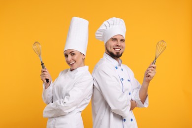 Photo of Happy professional confectioners in uniforms holding whisks on yellow background