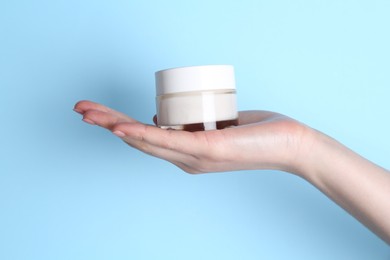 Woman holding jar of cream on light blue background, closeup