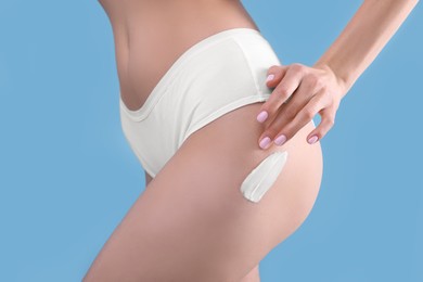 Photo of Woman with smear of body cream on her leg against light blue background, closeup