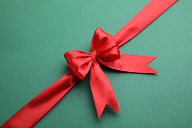 Photo of Red satin ribbon with bow on green background, top view