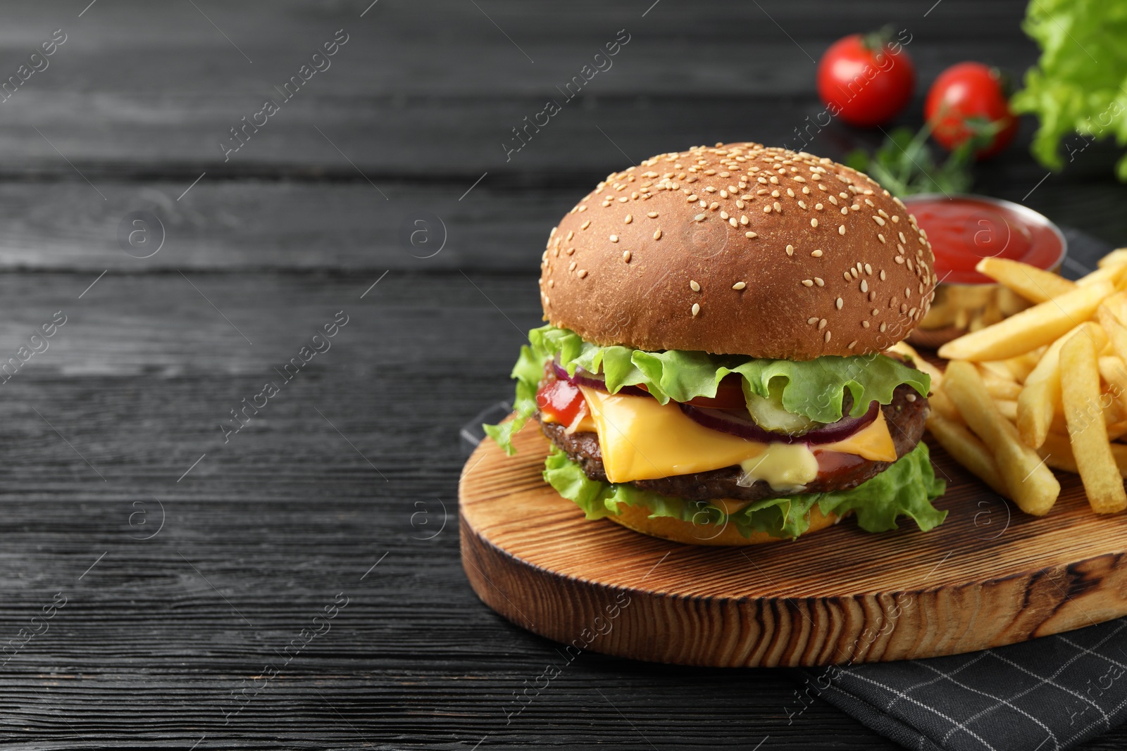 Photo of Delicious burger with beef patty, tomato sauce and french fries on black wooden table, space for text