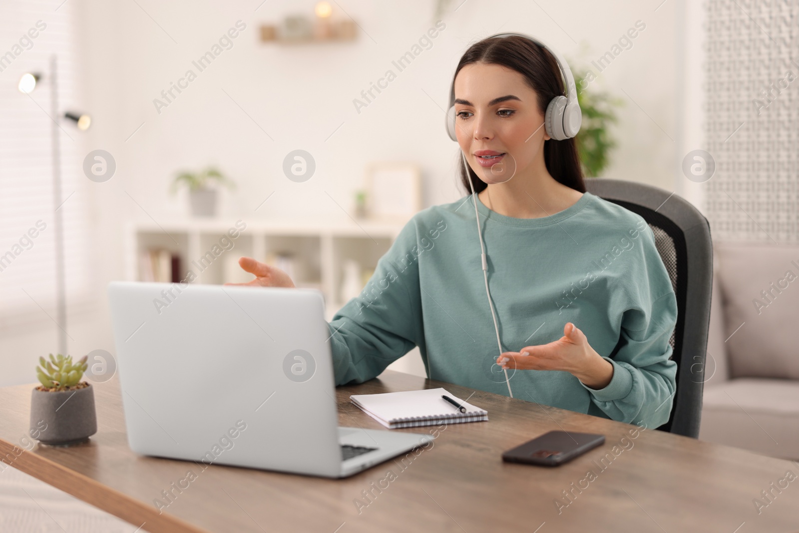 Photo of Young woman in headphones using video chat during webinar at table in room