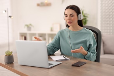 Photo of Young woman in headphones using video chat during webinar at table in room