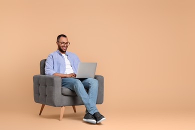 Photo of Smiling young man working with laptop in armchair on beige background, space for text