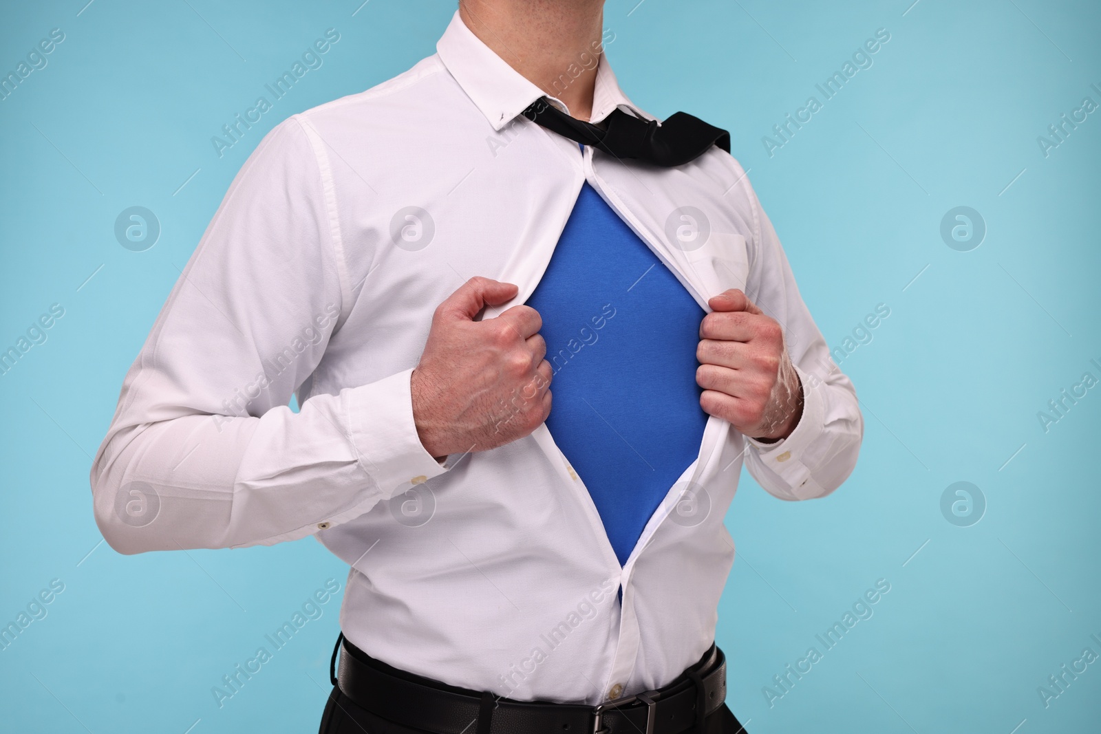 Photo of Businessman wearing superhero costume under suit on light blue background, closeup