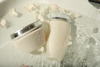 Photo of Hair care cosmetic products with flower petals and water in sink, above view