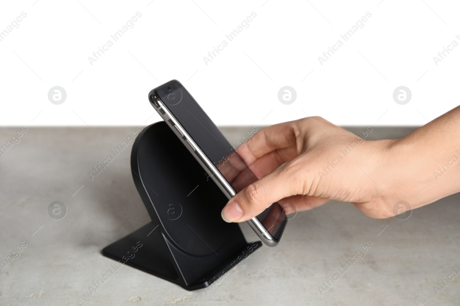 Photo of Woman putting mobile phone onto wireless charger at  grey table, closeup