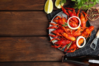 Flat lay composition with delicious red boiled crayfishes on wooden table, space for text