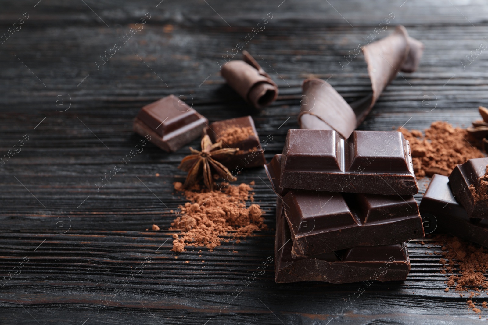 Photo of Pieces of black chocolate on wooden table. Space for text