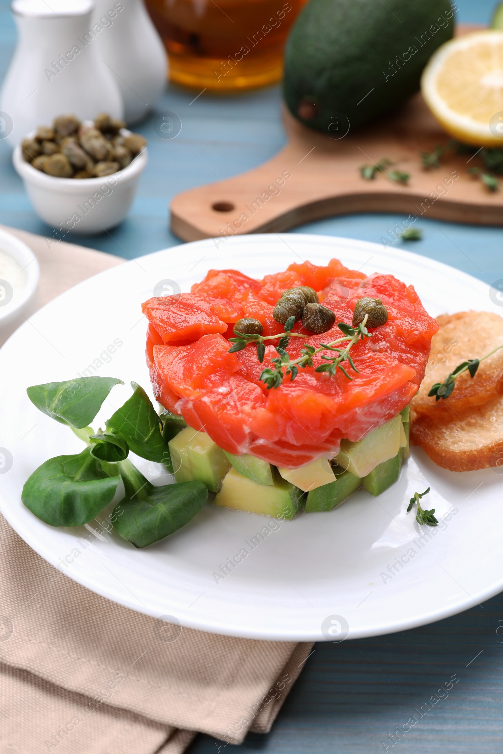 Photo of Delicious salmon tartare served with avocado and croutons on light blue table