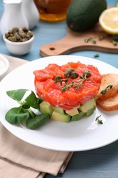 Delicious salmon tartare served with avocado and croutons on light blue table