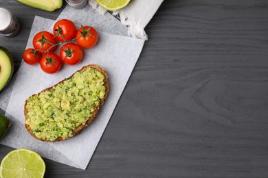 Photo of Delicious sandwich with guacamole, tomatoes and limes on gray wooden table, flat lay. Space for text