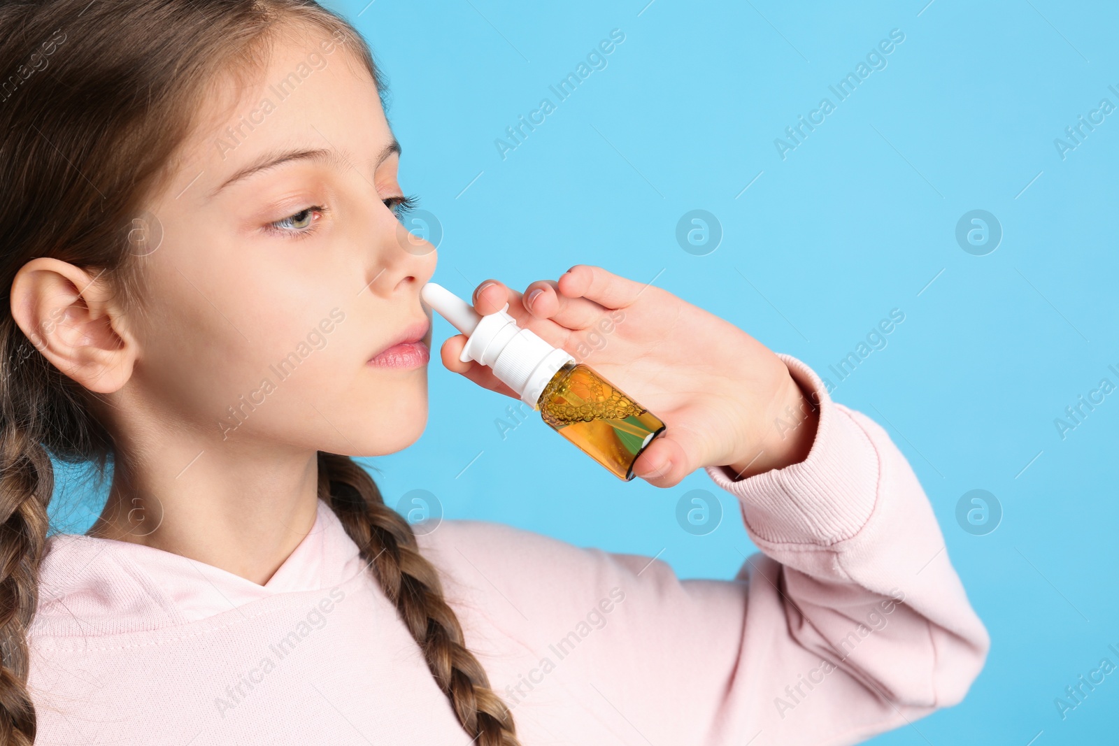 Photo of Sick little girl using nasal spray on light blue background