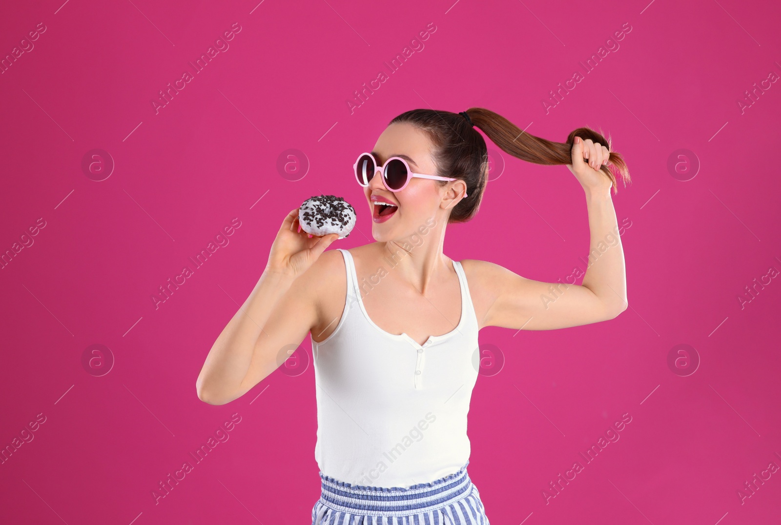 Photo of Beautiful young woman wearing sunglasses with donut on pink background