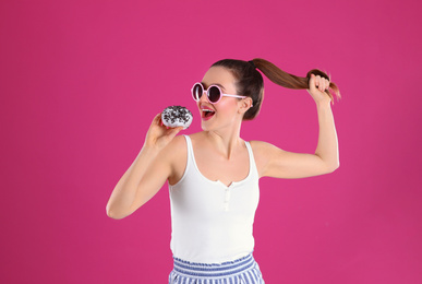 Beautiful young woman wearing sunglasses with donut on pink background