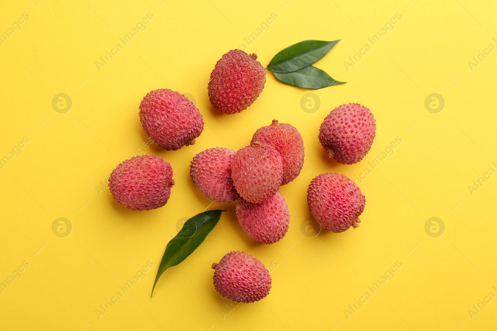 Photo of Fresh ripe lychees with leaves on yellow background, flat lay