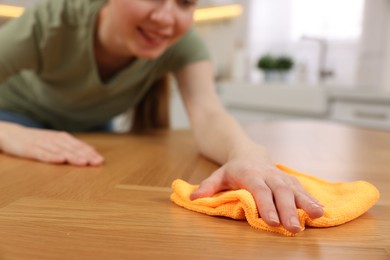 Photo of Woman with microfiber cloth cleaning wooden table in kitchen, closeup