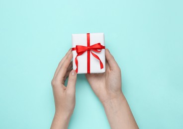 Photo of Woman holding beautiful gift box on turquoise background, top view