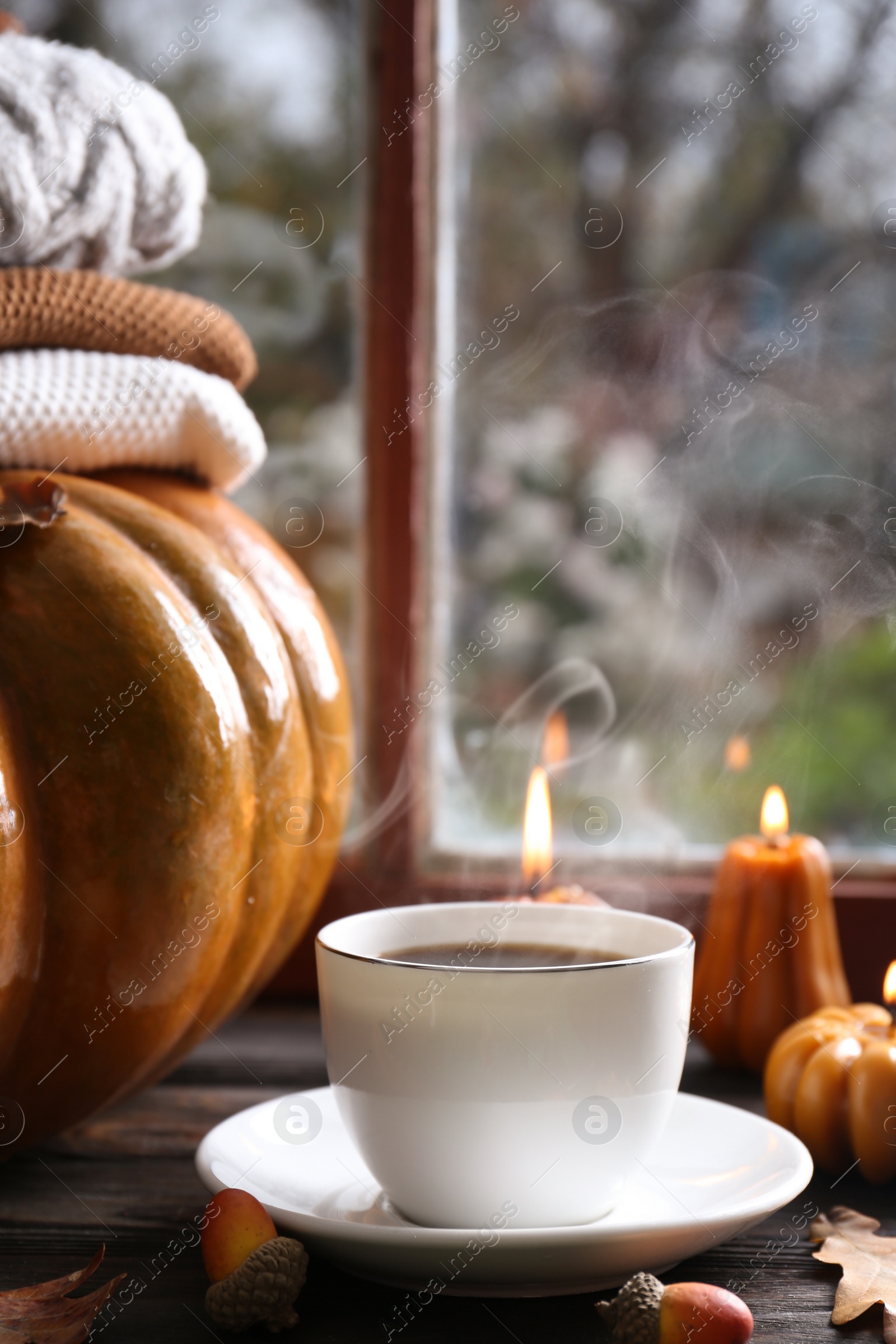 Photo of Cup of hot drink and pumpkin shaped candles on wooden table near window. Cozy autumn atmosphere