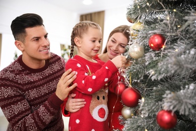 Happy family with cute child decorating Christmas tree together at home