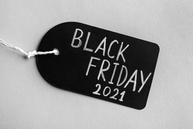 Photo of Tag with words BLACK FRIDAY 2021 on light background, top view