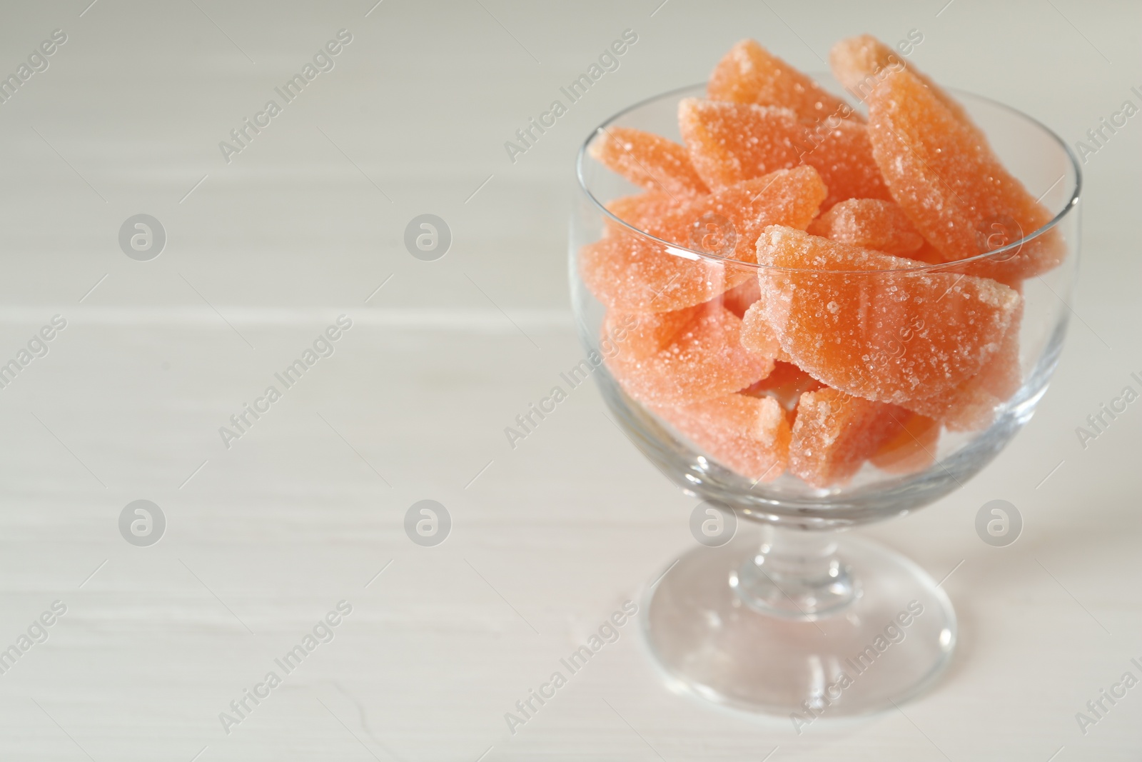 Photo of Tasty orange jelly candies in glass dessert bowl on white table. Space for text