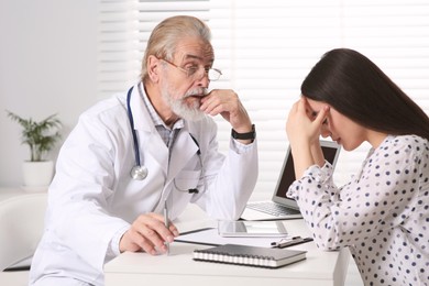 Photo of Senior doctor consulting patient at white table in clinic
