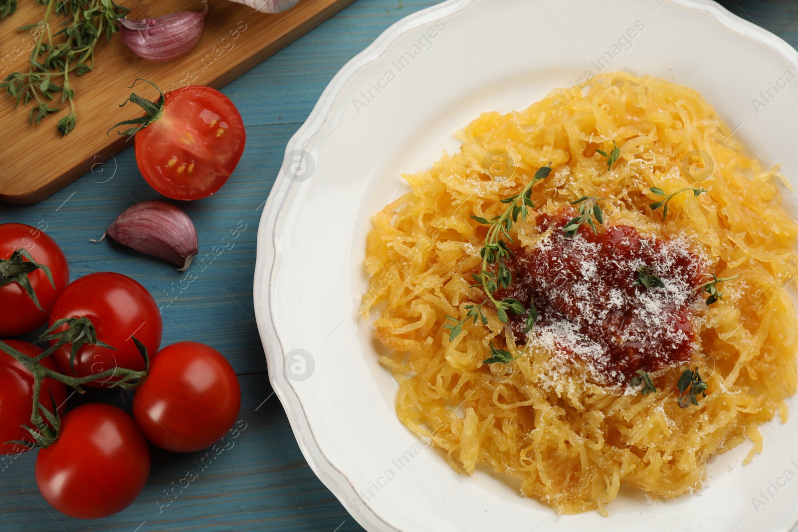 Photo of Tasty spaghetti squash with tomato sauce, cheese and thyme served on light blue wooden table, flat lay