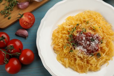 Photo of Tasty spaghetti squash with tomato sauce, cheese and thyme served on light blue wooden table, flat lay