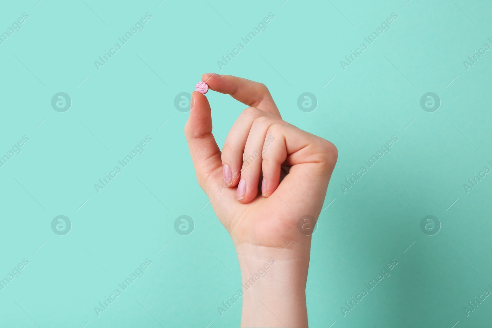 Photo of Woman holding vitamin pill on turquoise background, closeup