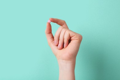 Photo of Woman holding vitamin pill on turquoise background, closeup