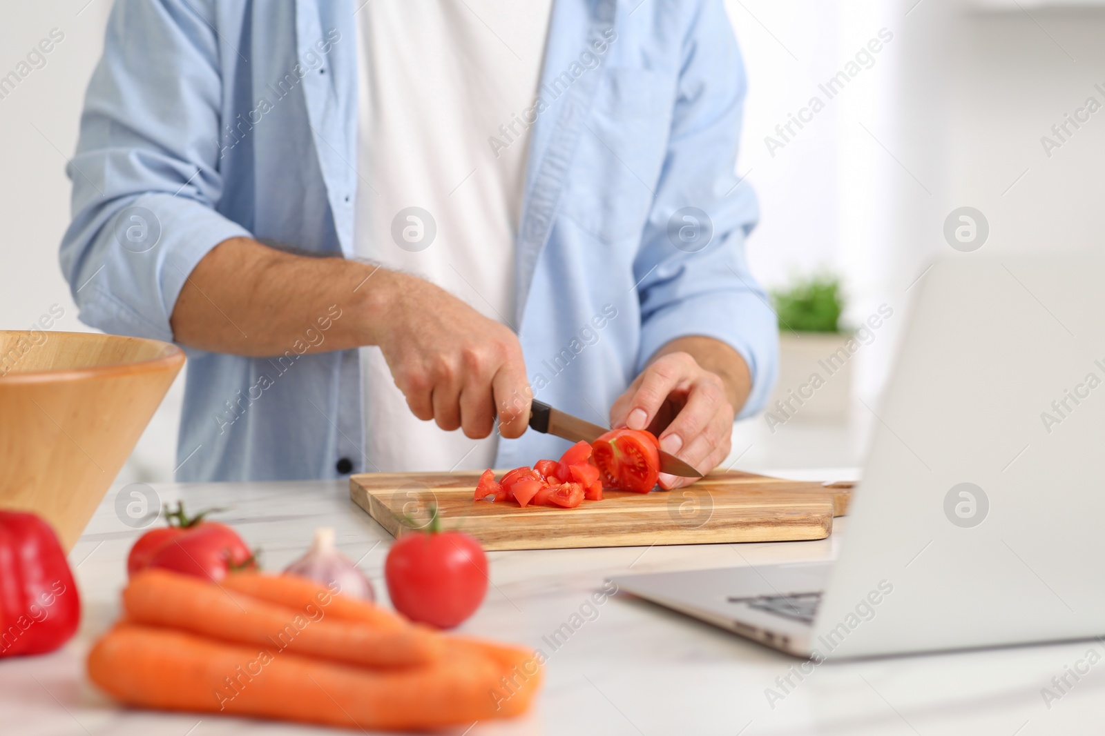 Photo of Man making dinner while watching online cooking course via laptop in kitchen, closeup