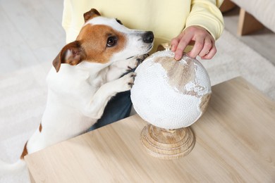 Woman pointing at globe near dog indoors, closeup. Travel with pet concept