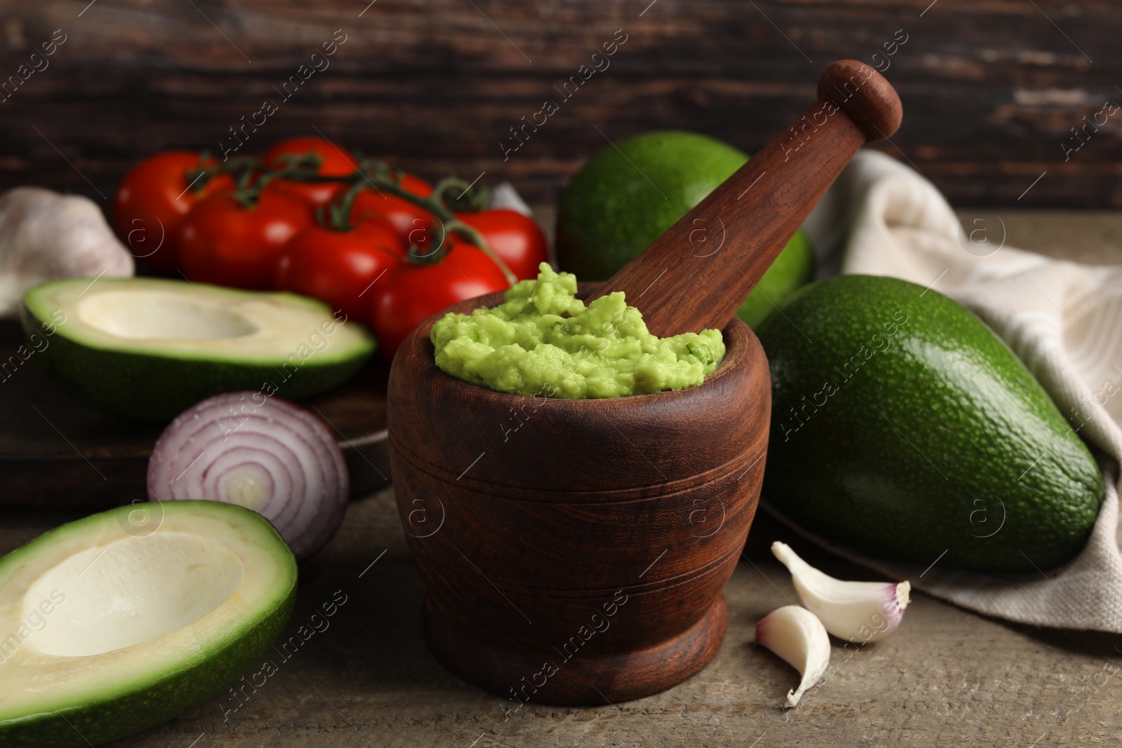 Photo of Mortar with delicious guacamole and ingredients on wooden table